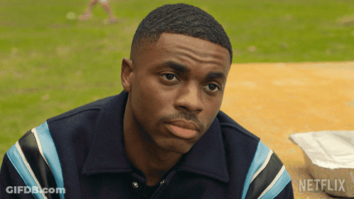 A Man Is Sitting At A Table With A Box Of Netflix Behind Him GIF