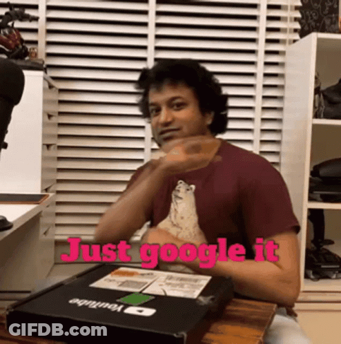 A Man Is Sitting At A Table With A Box That Says Just Google It GIF