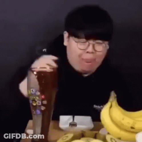 A Man Is Sitting At A Table With A Bunch Of Bananas And A Glass Of Beer . GIF