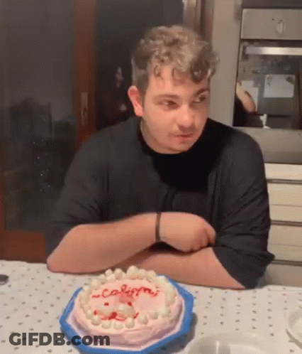 A Man Is Sitting At A Table With A Cake On It And Looking At It . GIF