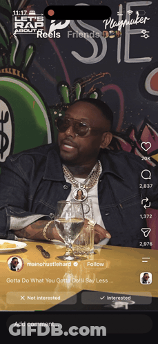 A Man Is Sitting At A Table With A Glass Of Water In Front Of A Sign That Says Playmaker GIF