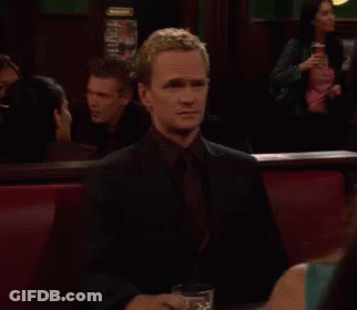 A Man Is Sitting At A Table With A Glass Of Whiskey In Front Of Him GIF