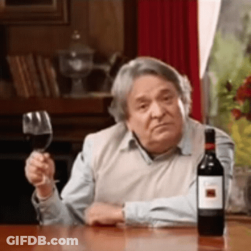 A Man Is Sitting At A Table With A Glass Of Wine And A Bottle Of Wine . GIF