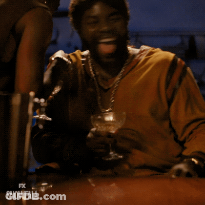 A Man Is Sitting At A Table With A Glass Of Wine In His Hand And The Words Fx Snowfall On The Bottom Right GIF