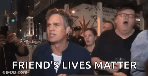 A Man Is Sitting At A Table With A Group Of People And The Words `` Friend 'S Lives Matter '' Written On It . GIF