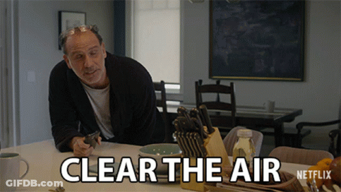 A Man Is Sitting At A Table With A Knife Holder And A Sign That Says Clear The Air GIF