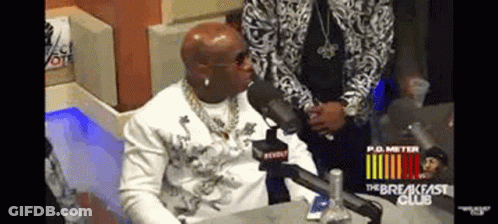 A Man Is Sitting At A Table With A Microphone In Front Of Him . GIF