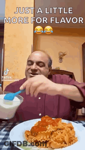A Man Is Sitting At A Table With A Plate Of Pasta And A Spoon . GIF