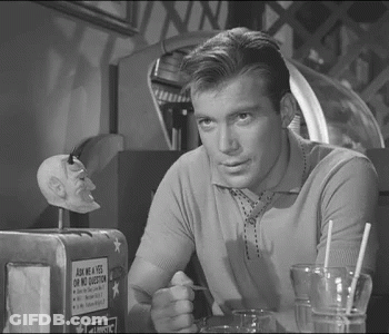 A Man Is Sitting At A Table With A Sign That Says Ask Me A Yes On No Question GIF
