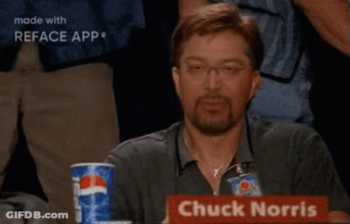 A Man Is Sitting At A Table With A Sign That Says Chuck Norris On It GIF