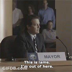 A Man Is Sitting At A Table With A Sign That Says Mayor On It GIF