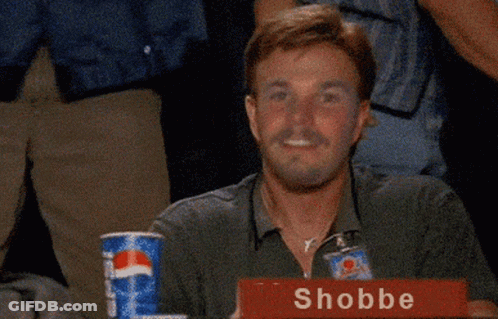 A Man Is Sitting At A Table With A Sign That Says Shobbe On It GIF