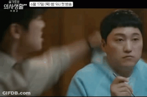 A Man Is Sitting At A Table With Chopsticks In His Hand And Another Man Is Standing Next To Him . GIF