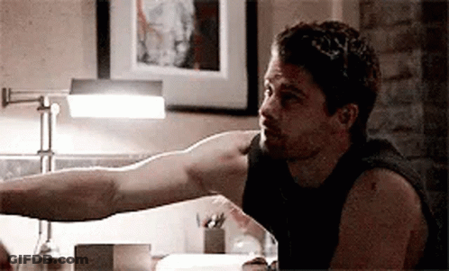 A Man Is Sitting At A Table With His Arm Outstretched In Front Of A Lamp . GIF