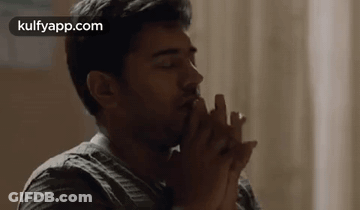 A Man Is Sitting At A Table With His Hands Folded In Front Of His Face . GIF
