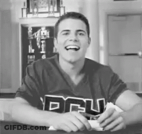 A Man Is Sitting At A Table With His Mouth Open And Smiling . He Is Wearing A Shirt With The Word Dru On It . GIF