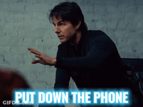 A Man Is Sitting At A Table With The Words Put Down The Phone Above Him GIF