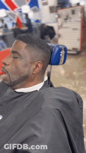 A Man Is Sitting In A Barber Chair With His Eyes Closed . GIF