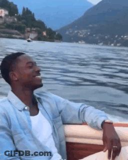 A Man Is Sitting In A Boat On A Lake GIF