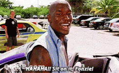 A Man Is Sitting In A Car In A Parking Lot And Laughing While A Man Stands In The Background . GIF