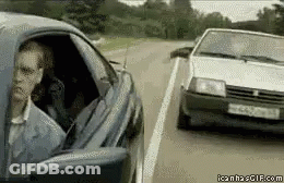 A Man Is Sitting In A Car Looking Out The Window While Another Car Drives Past Him . GIF