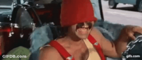 A Man Is Sitting In A Car Wearing A Red Hat And Overalls . GIF