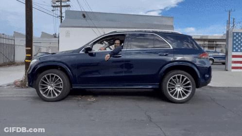 A Man Is Sitting In A Car With His Hand Out The Window GIF