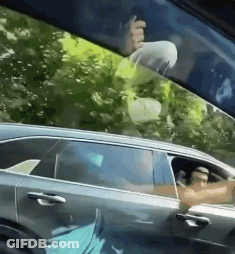 A Man Is Sitting In A Car With His Head Out The Window . GIF