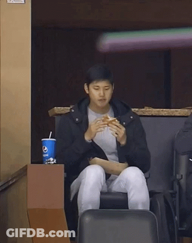 A Man Is Sitting In A Chair Eating A Hamburger And Drinking Pepsi . GIF