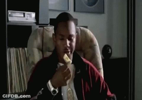 A Man Is Sitting In A Chair Eating A Piece Of Banana . GIF