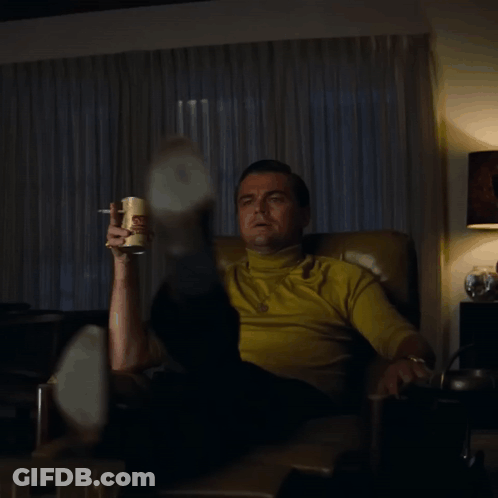 A Man Is Sitting In A Chair Holding A Can Of Potato Chips And Smoking A Cigarette GIF