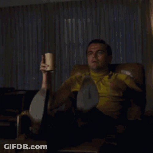 A Man Is Sitting In A Chair Holding A Cup Of Coffee And Pointing At Something With The Words Look A Slacker Written Belo GIF
