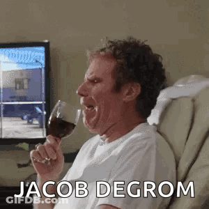 A Man Is Sitting In A Chair Holding A Glass Of Wine And Making A Funny Face . GIF