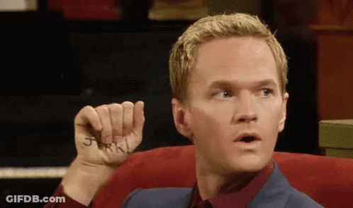 A Man Is Sitting In A Chair Holding A Piece Of Paper With The Word Jerk Written On His Hand . GIF