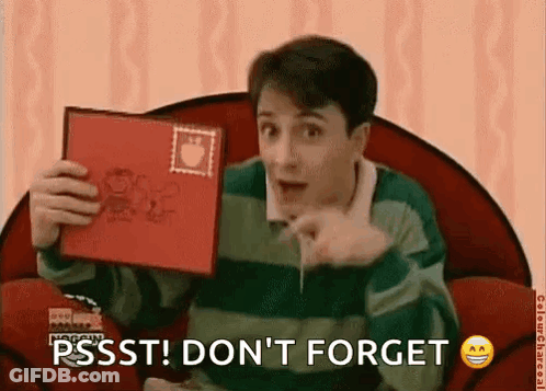 A Man Is Sitting In A Chair Holding A Red Book And Pointing At The Camera . GIF