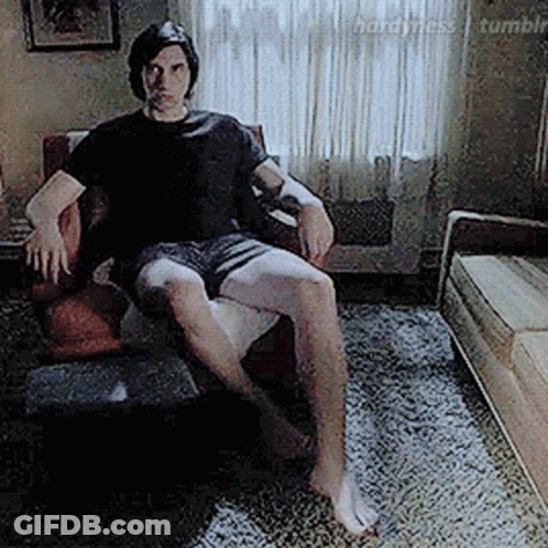 A Man Is Sitting In A Chair In A Living Room Without A Shirt On . GIF