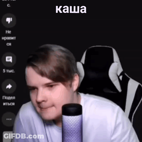 A Man Is Sitting In A Chair In Front Of A Microphone With A Foreign Language On The Screen . GIF