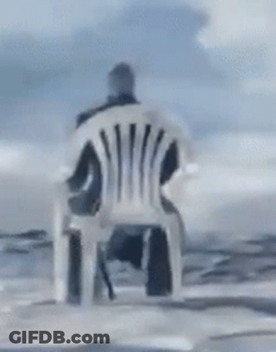 A Man Is Sitting In A Chair In Front Of The Ocean GIF