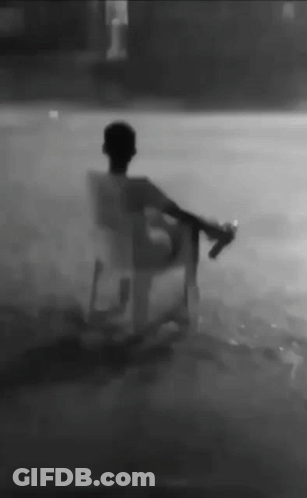 A Man Is Sitting In A Chair In The Rain Holding A Bottle . GIF
