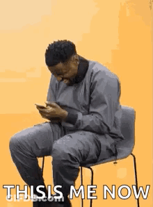 A Man Is Sitting In A Chair Looking At His Cell Phone And Saying `` This Is Me Now '' . GIF