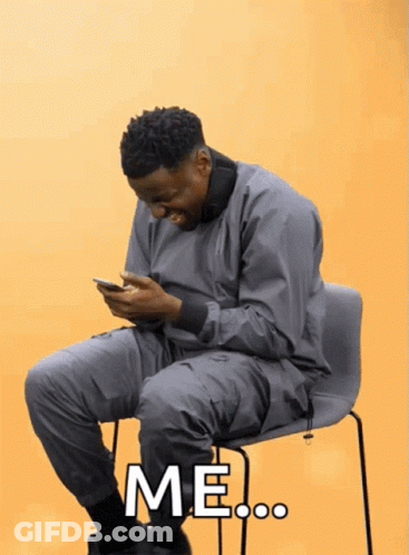 A Man Is Sitting In A Chair Looking At His Phone And The Word Me Is On The Screen GIF