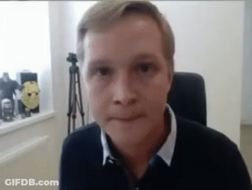 A Man Is Sitting In A Chair Looking At The Camera And Making A Face . GIF