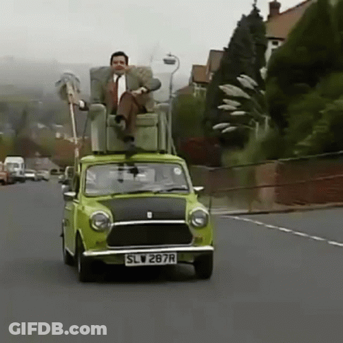 A Man Is Sitting In A Chair On Top Of A Green Car . GIF