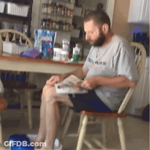 A Man Is Sitting In A Chair Reading A Book GIF
