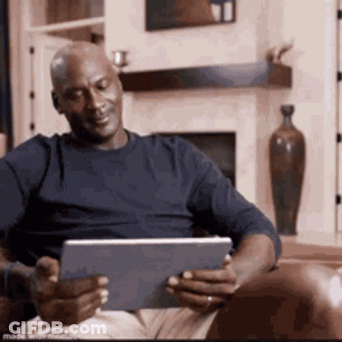 A Man Is Sitting In A Chair Using A Tablet Computer . GIF