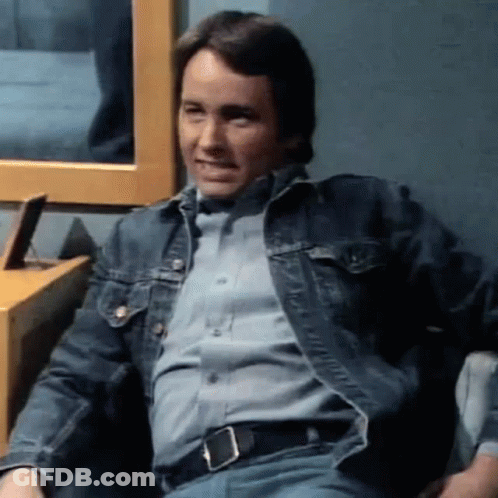 A Man Is Sitting In A Chair Wearing A Denim Jacket And A Blue Shirt . GIF