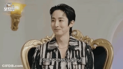 A Man Is Sitting In A Chair Wearing A Striped Shirt And A Necklace . GIF