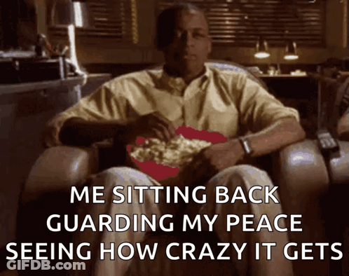 A Man Is Sitting In A Chair With A Bowl Of Popcorn On His Lap And The Caption Says Me Sitting Back Guarding My Peace GIF