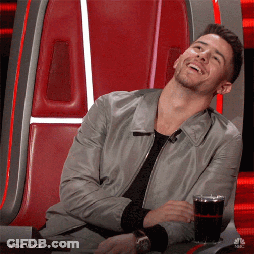 A Man Is Sitting In A Chair With A Glass Of Soda In Front Of Him And The Words #Thevoice Are On The Bottom GIF