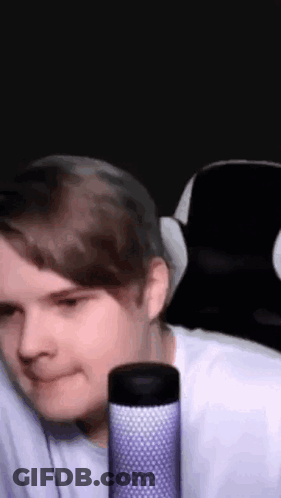 A Man Is Sitting In A Chair With A Microphone In Front Of Him And Smiling . GIF